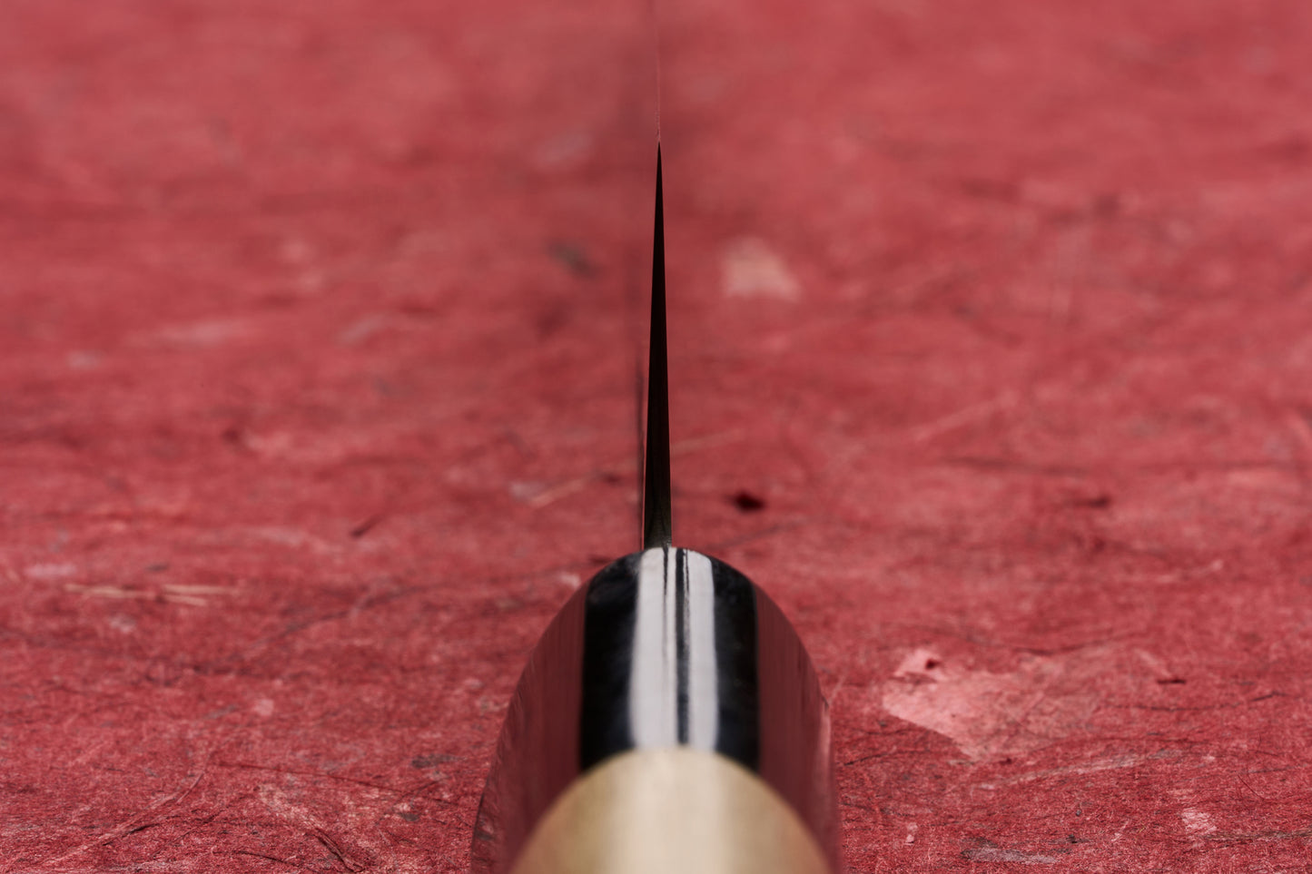 Masamoto KS Hongasumi Petty 165mm knife blade, captured in an edge-on close-up against a red textured background, showcases its precision and thinness, ideal for detailed kitchen tasks.