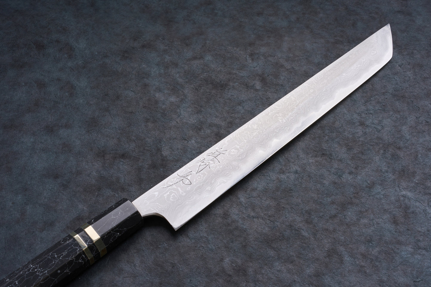Mazaki Aogami Super Honsanmai Damascus Sakimaru Sujihiki 300mm knife with patterned Damascus steel, etched kanji, and a black octagonal handle with brass bands.