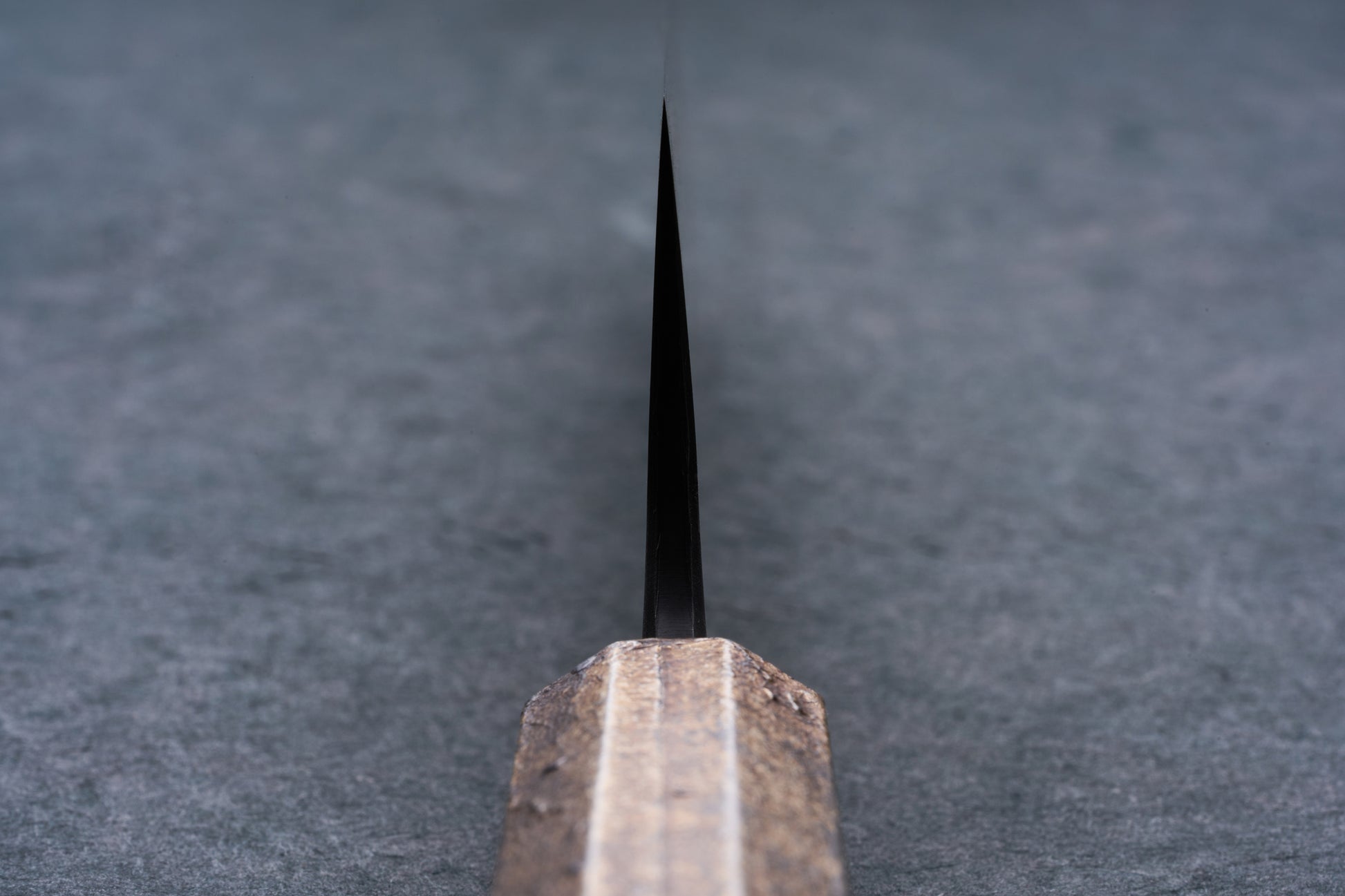 Mazaki Aoichi Beads Black Damascus Gyuto 240mm knife blade emerging from a wooden handle, set on a gray surface, showcasing Japanese craftsmanship.