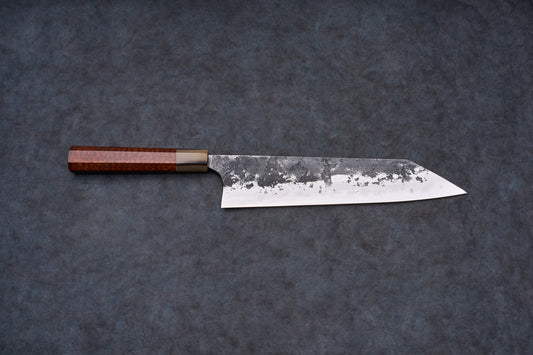 Mazaki Aoichi Honsanmai Kurouchi Nashiji Kiritsuke Gyuto 240mm with a hammered blade and octagonal wooden handle displayed on a textured surface.