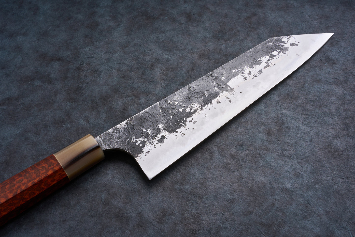 Mazaki Aoichi Honsanmai Kurouchi Nashiji Kiritsuke Gyuto 240mm knife on slate surface, featuring a hammered steel blade and wooden handle with metal ferrule.