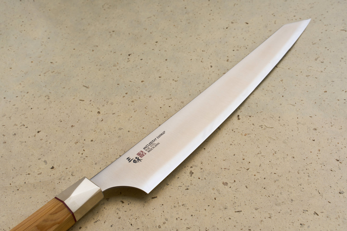 Mcusta Zanmai Beyond Kiritsuke Sujihiki 270mm knife displayed flat on a countertop, highlighting its long, single-bevel blade and Hinoki wood handle, ideal for precision slicing of fish and meats.