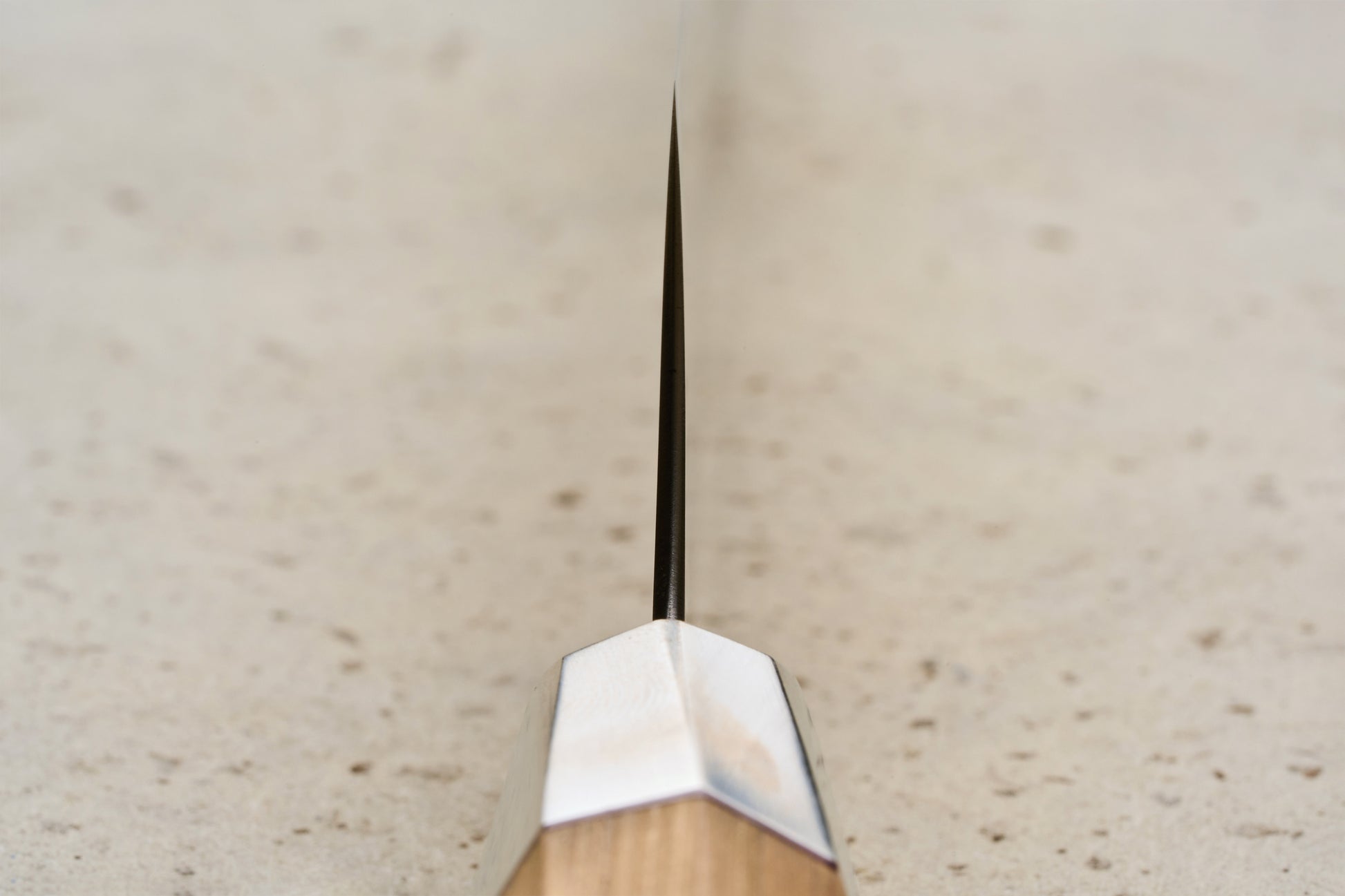 Mcusta Zanmai Beyond Kiritsuke Sujihiki 270mm knife, showcasing a thin blade with a metal bolster and a Hinoki wood handle, resting on a speckled stone-like surface, embodying luxury and precision craftsmanship.