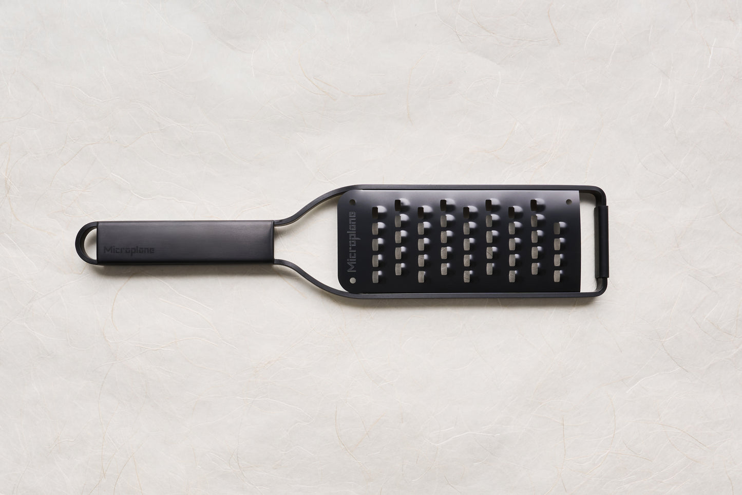 Microplane Black Sheep Series Grater, featuring a sleek black design, long handle, and perforated stainless-steel surface, ideal for grating hard cheeses, citrus, and spices with precision and ease.