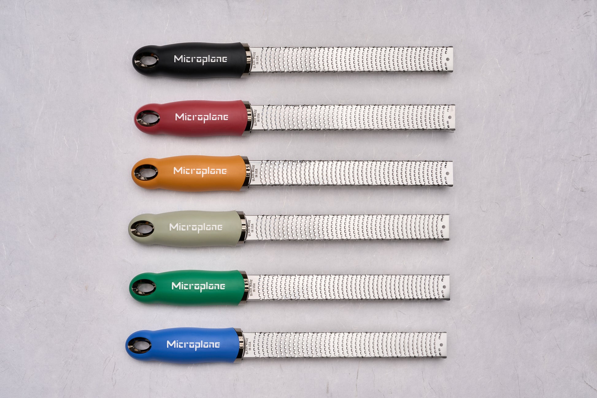 Six Microplane Premium Classic Zesters with fine-toothed stainless-steel blades and colorful soft-grip handles, perfect for zesting citrus and grating cheeses with precision, enhancing any culinary toolkit.