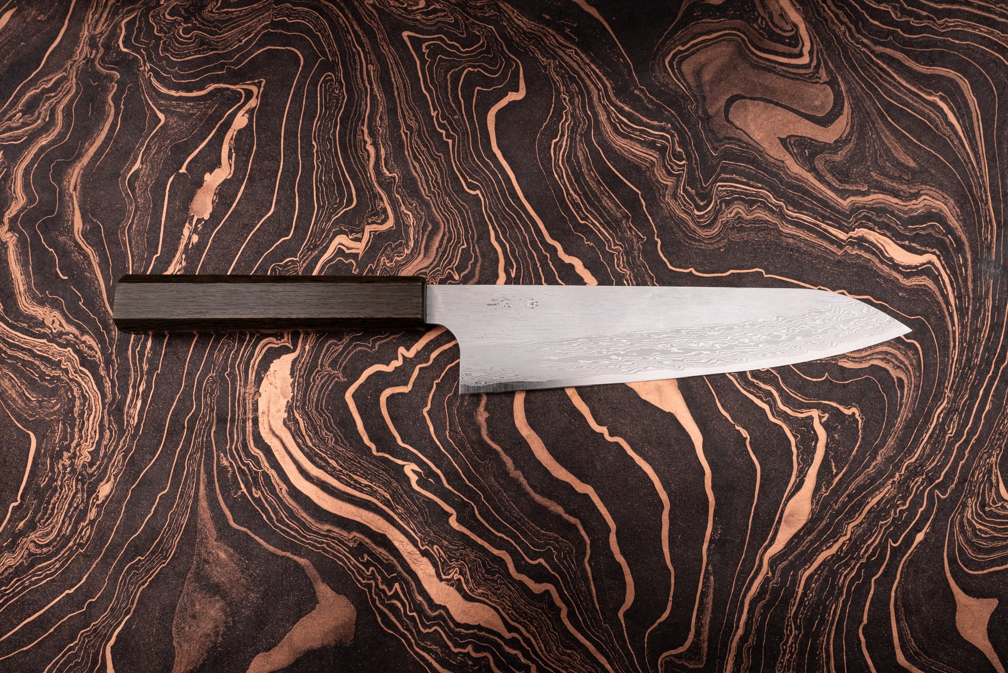 Nigara VG XEOS Tsuchime Damascus Gyuto 225mm with a Damascus-patterned blade and dark wooden octagonal handle, displayed on a marbled surface, epitomizing Japanese craftsmanship and versatility for culinary enthusiasts.