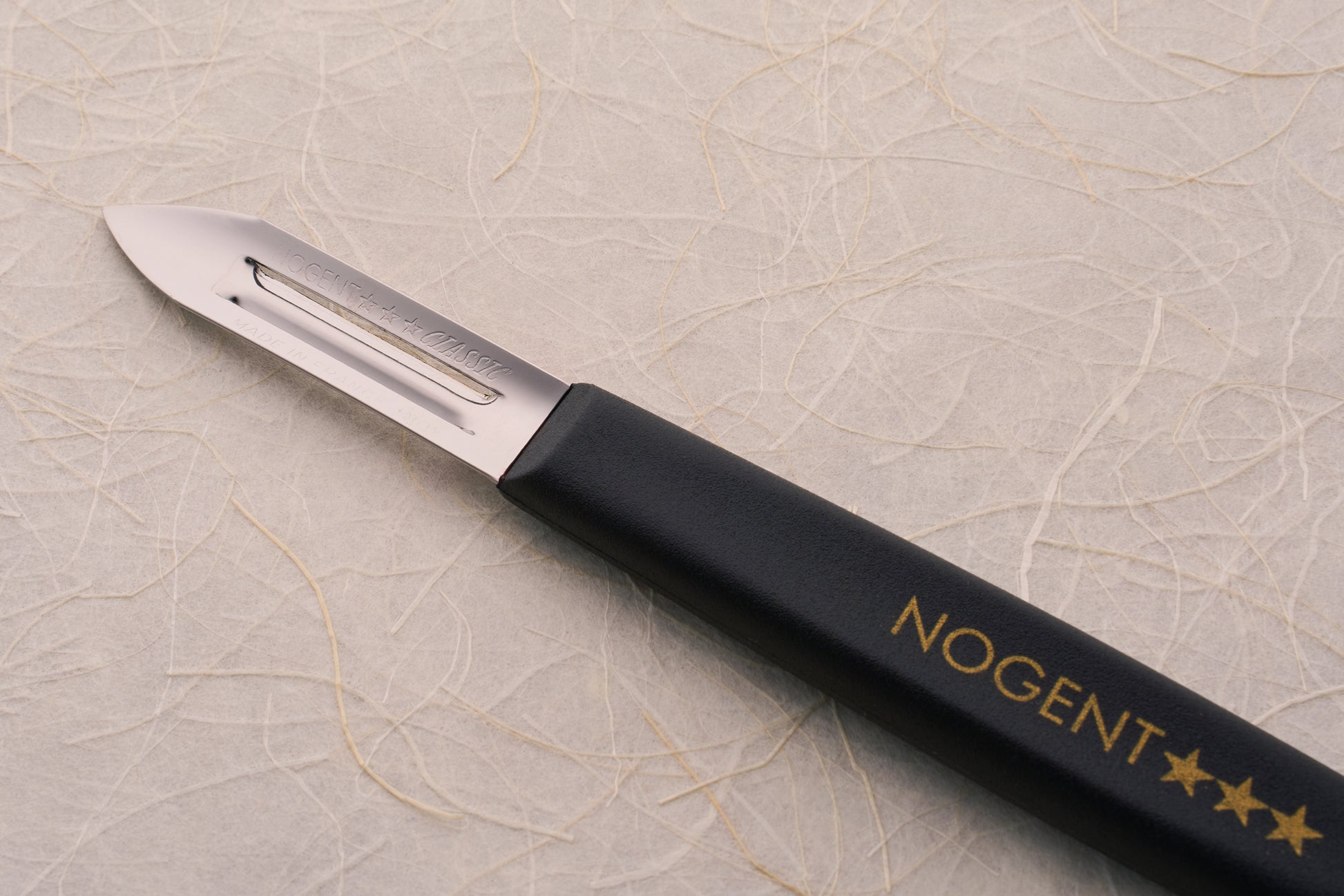 Nogent Double Edge Peeler with stainless steel blade and black handle, showcasing NOGENT branding, ideal for precise, dual-directional peeling; reflecting high-quality craftsmanship.