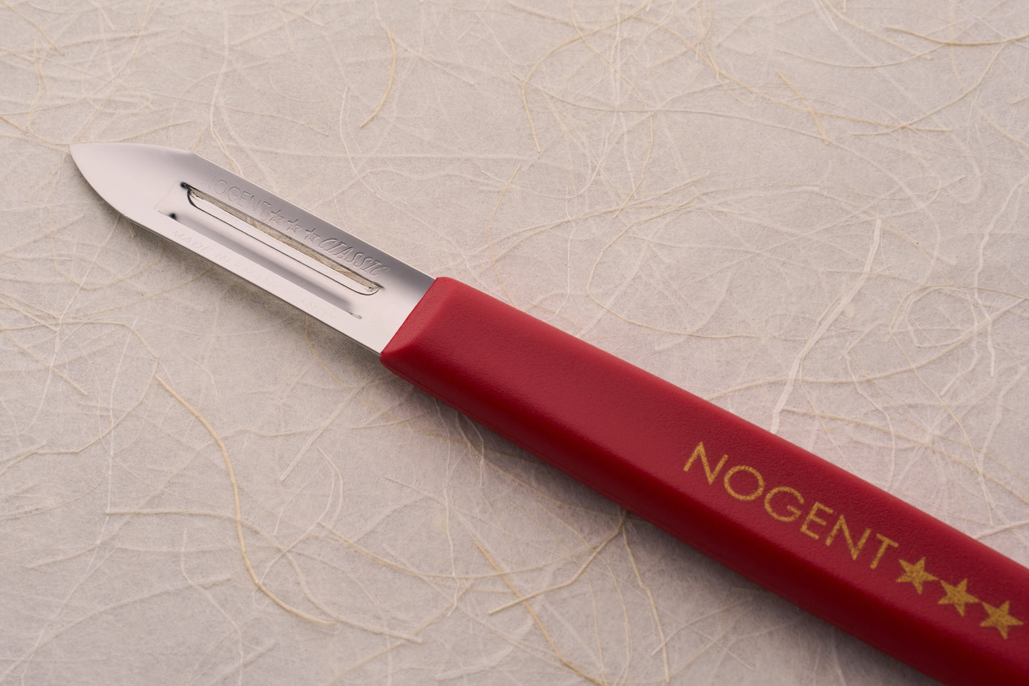 Nogent Double Edge Peeler with a red handle, featuring a stainless-steel blade for efficient, dual-direction peeling; brand stamped in gold, made in France.