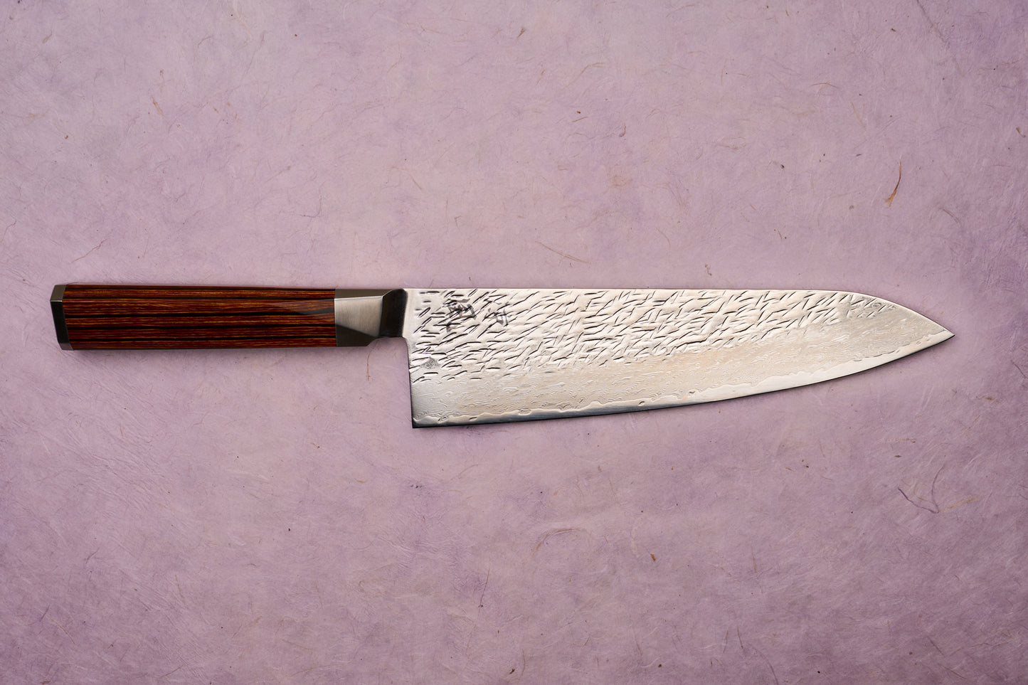 Ono Knife Suzukaze SG2 Tsuchime Damascus Gyuto 210mm, featuring a hammered Damascus blade and octagonal wooden handle, against a pale mauve background, embodies precision craftsmanship and cutting-edge technology.