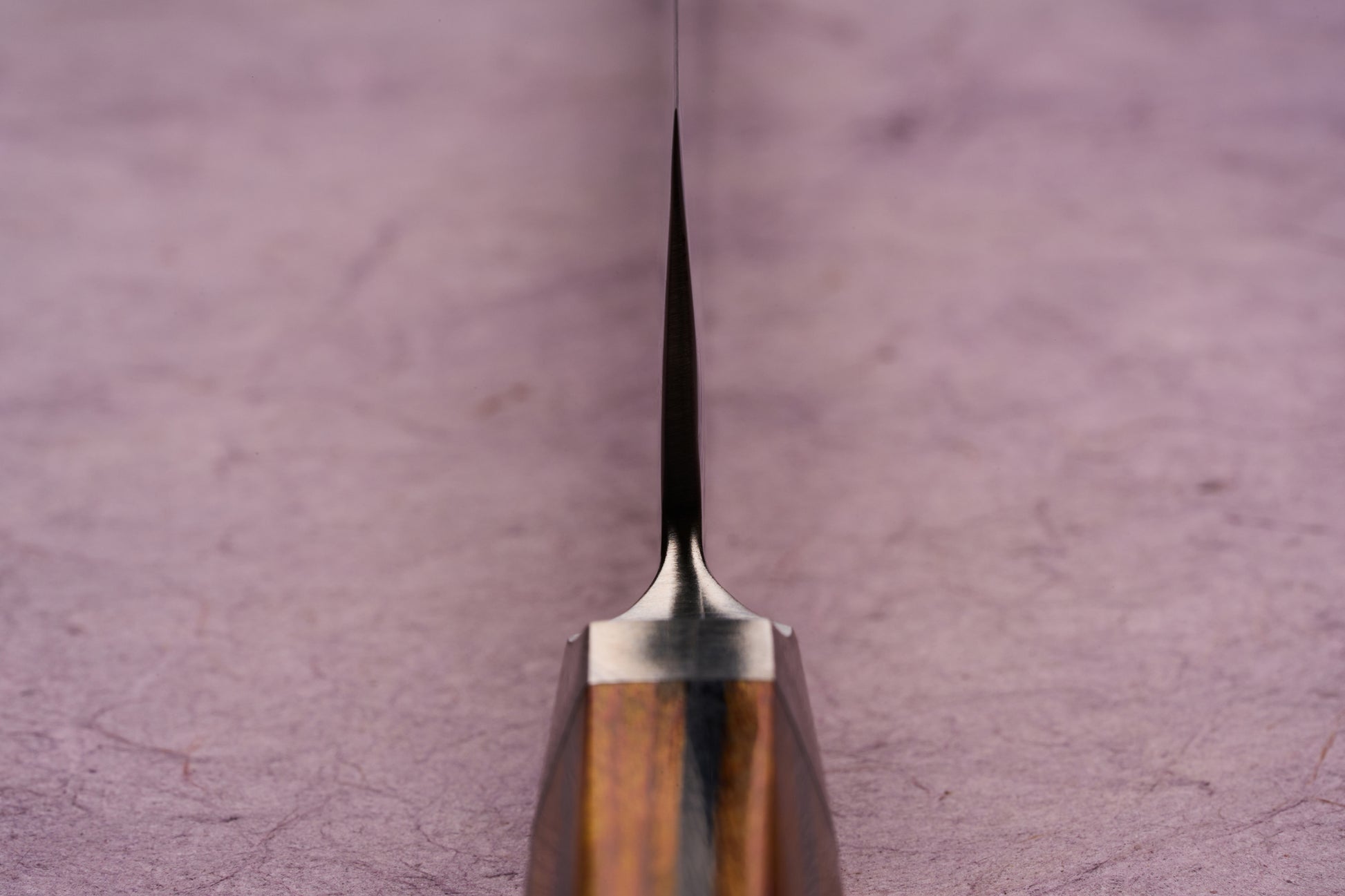 Ono Knife Suzukaze SG2 Tsuchime Damascus Petty 150mm, viewed from the handle, showcases its thin, tapering blade. The wooden handle and metal bolster subtly visible, highlight craftsmanship and precision.