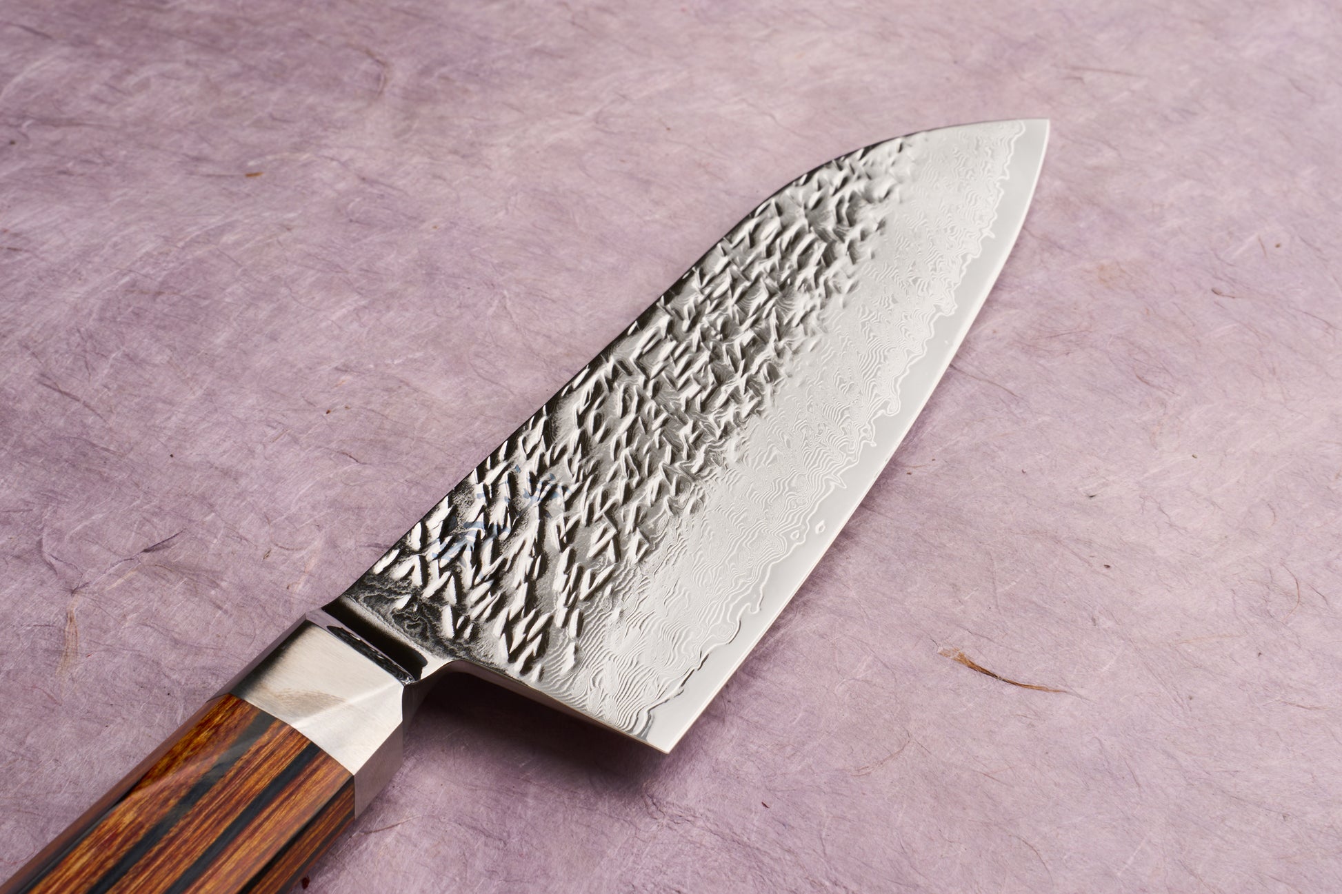 Ono Knife Suzukaze SG2 Tsuchime Damascus Santoku 180mm features a hammered blade with a Damascus wave pattern and a striped wood handle, embodying precision craftsmanship ideal for versatile kitchen tasks.