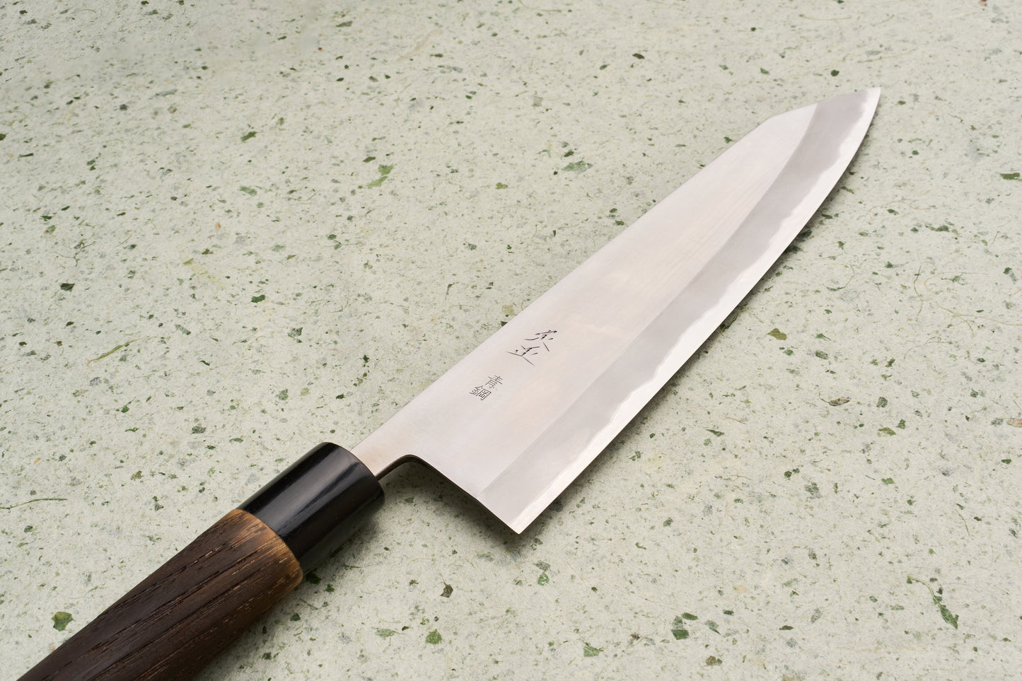 Sadamasa Aogami Stainless Migaki Kiritsuke Gyuto 240mm features a long, single-bevel blade with a hamon line and Japanese characters, complemented by an octagonal wooden handle, displayed on a speckled countertop.