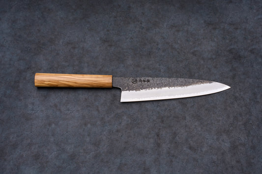 Sakai Takayuki Sanpo Mizu Gyuto 210mm knife with an octagonal wooden handle and a tsuchime-textured, polished steel blade on a slate surface.