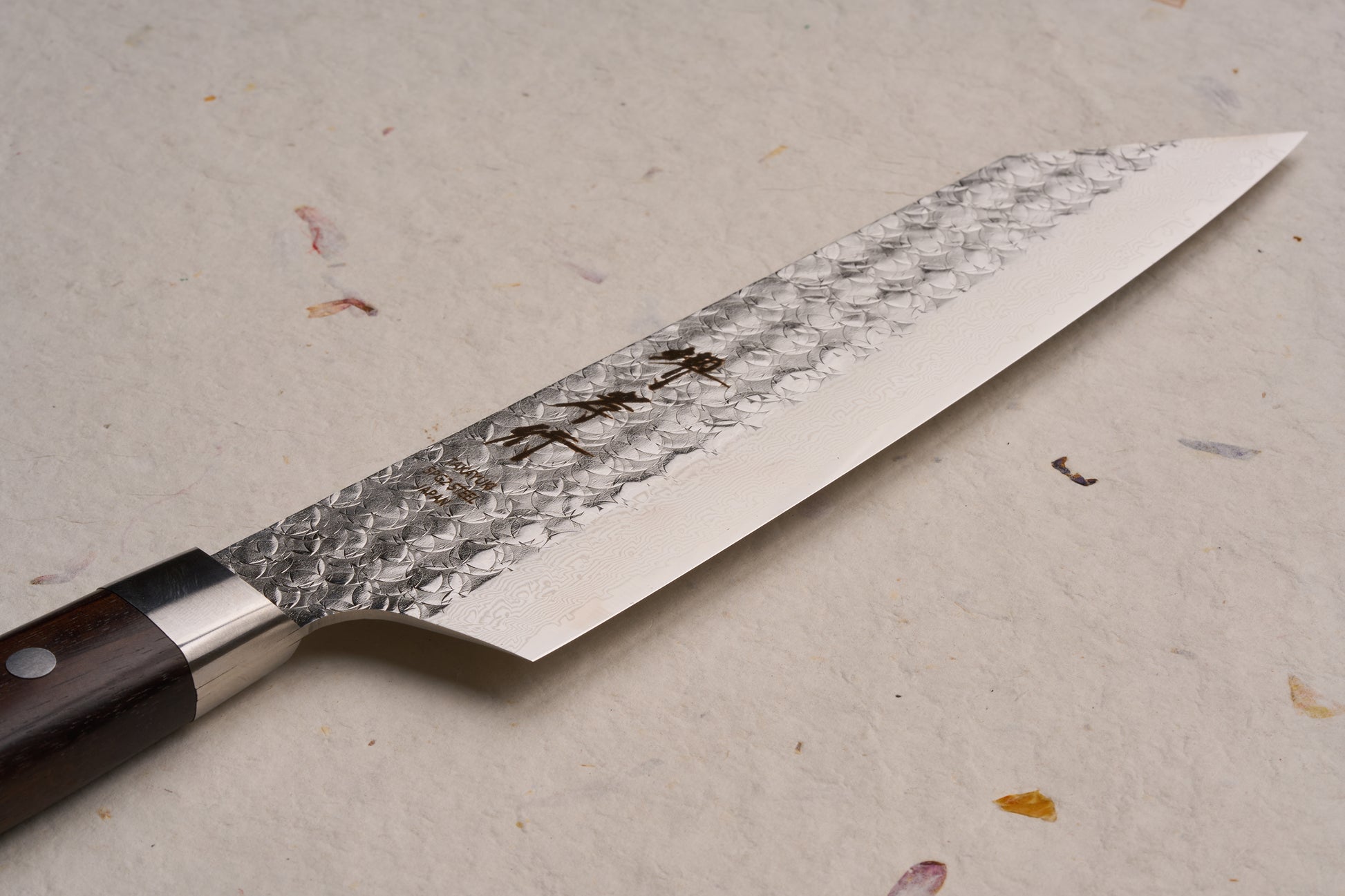 Sakai Takayuki SG2 Tsuchime Damascus Western Kengata Gyuto 190mm features a hammered Damascus blade with kanji engravings and a dark wood handle, embodying expert craftsmanship for versatile culinary use.