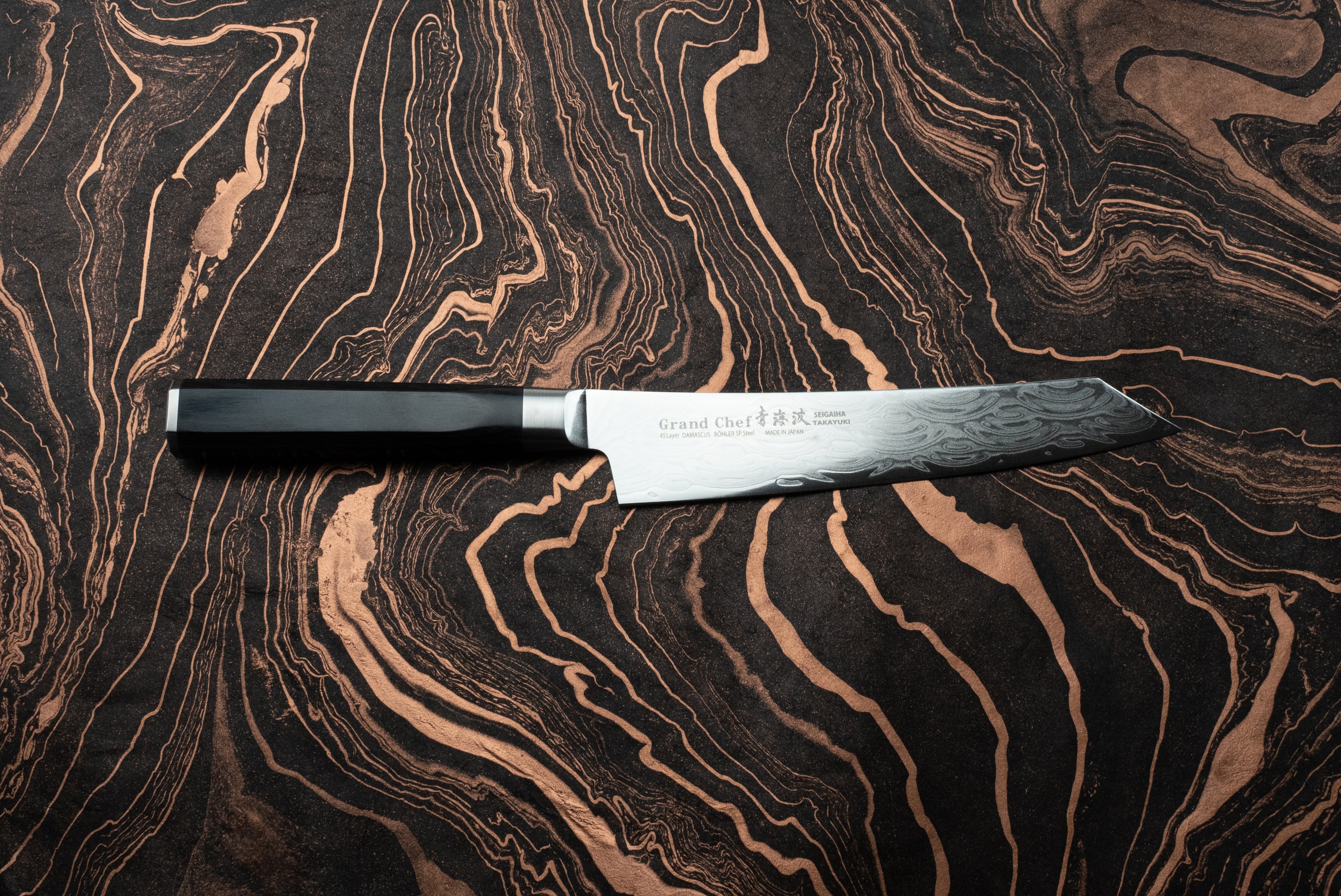 Sakai Takayuki Grand Chef Seigaiha Kengata Petty 150mm knife, featuring a 45-layer Damascus-pattern blade and black octagonal handle, displayed on a dark, marbled surface with coppery swirls.