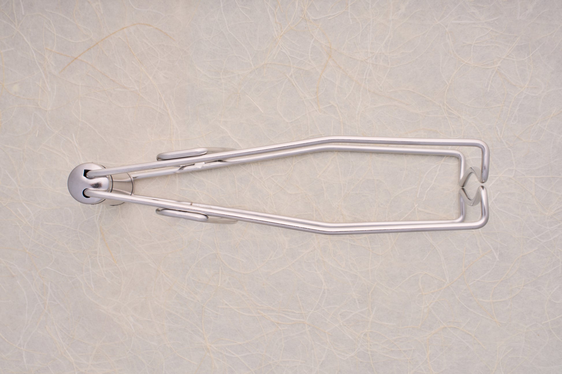 Shimoyama Stainless Steel Dish Clip Lifter, a sleek, wall-mounted, fold-out towel holder against a textured wall, exemplifying functional elegance in kitchen accessories.