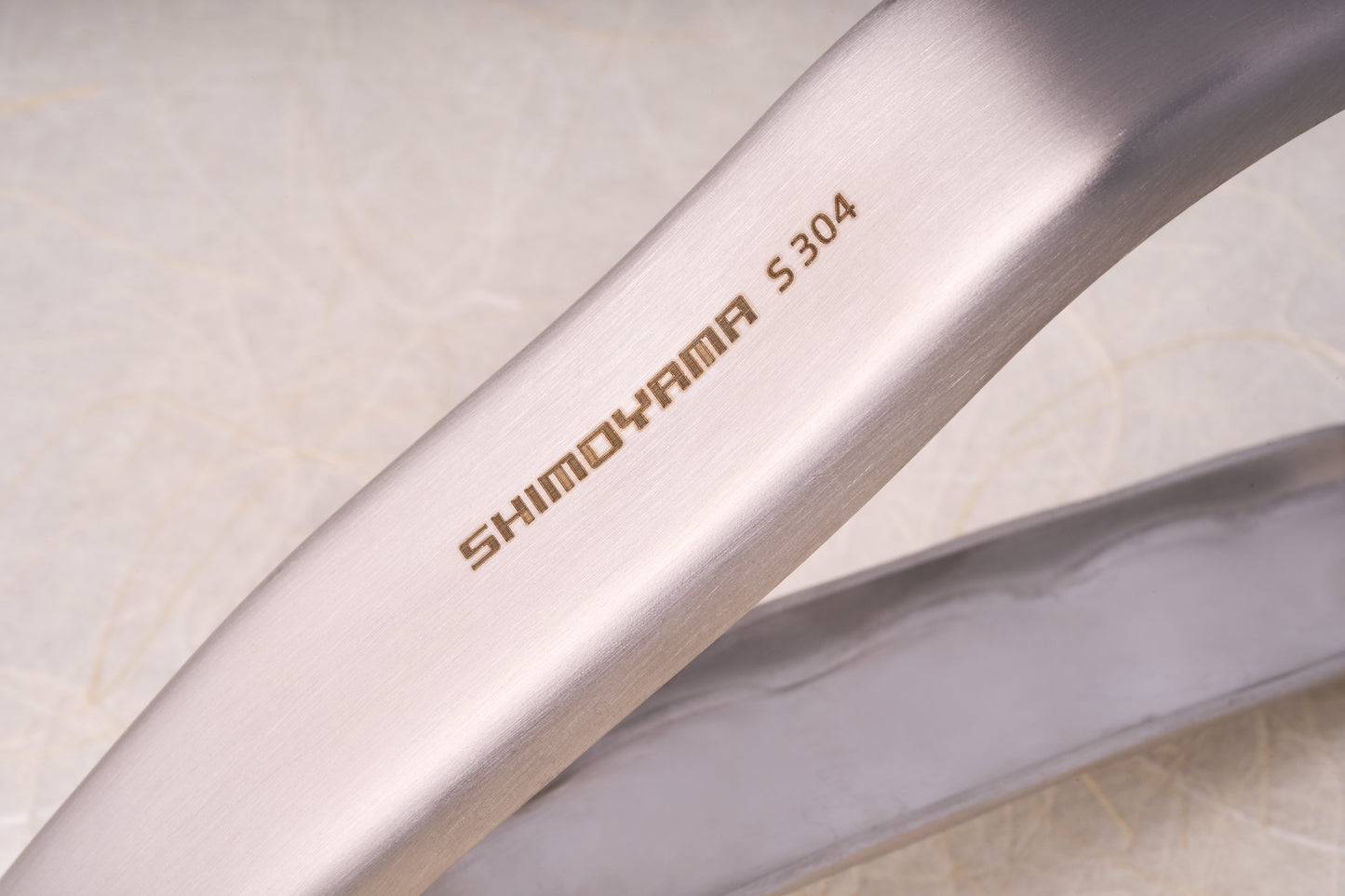 Close-up of Shimoyama Stainless Steel Bowl Clip, showcasing etched SHIMOHAMA S304 on brushed stainless steel, highlighting its fine grain and gentle curve.