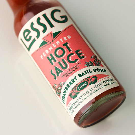 Bottle of “Strawberry Basil Bomb” by Lessig Ferments, a 148 ml fermented hot sauce, featuring strawberry, basil, and habanero flavors, crafted in Edmonton, AB.