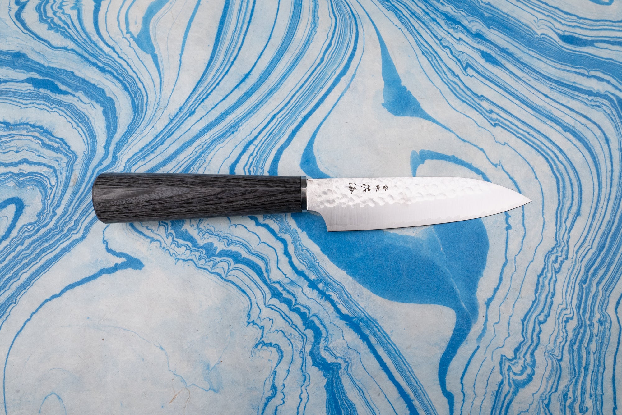 Touroku Sakai Gekka Petty 120mm knife with a hammered VG10 stainless steel blade and dark wooden handle, displayed on a marbled surface, showcasing fine Japanese craftsmanship and exceptional balance.