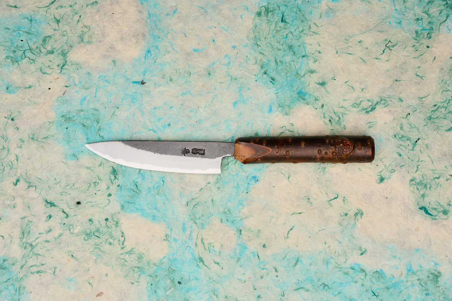 Tottori Otsuka Hamono Aoichi Kurouchi Petty 100mm knife with a single-bevel Aogami #1 steel blade, visible hammer marks, Japanese etchings, and a cylindrical bark-textured wooden handle.