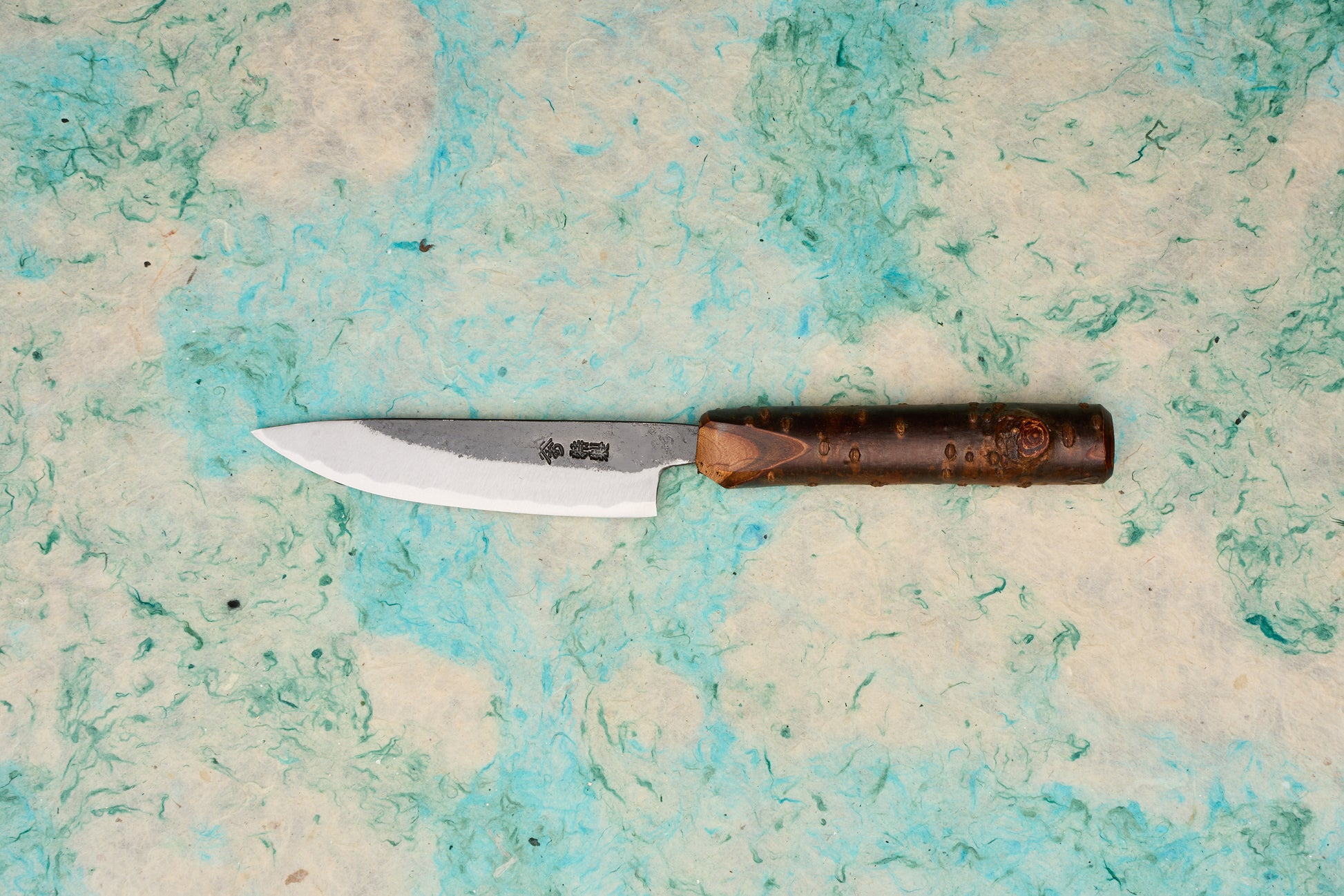 Tottori Otsuka Hamono Aoichi Kurouchi Petty 100mm knife with a single-bevel Aogami #1 steel blade, visible hammer marks, Japanese etchings, and a cylindrical bark-textured wooden handle.
