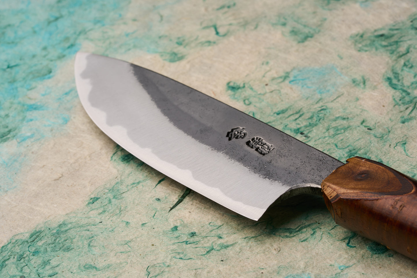Tottori Otsuka Hamono Aoichi Yamagoya Petty 125mm: Close-up of a gyuto-style knife, showcasing a polished blade with a hamon and a rustic cherrywood handle, exemplifying master blacksmith Otsuka-san's craftsmanship.