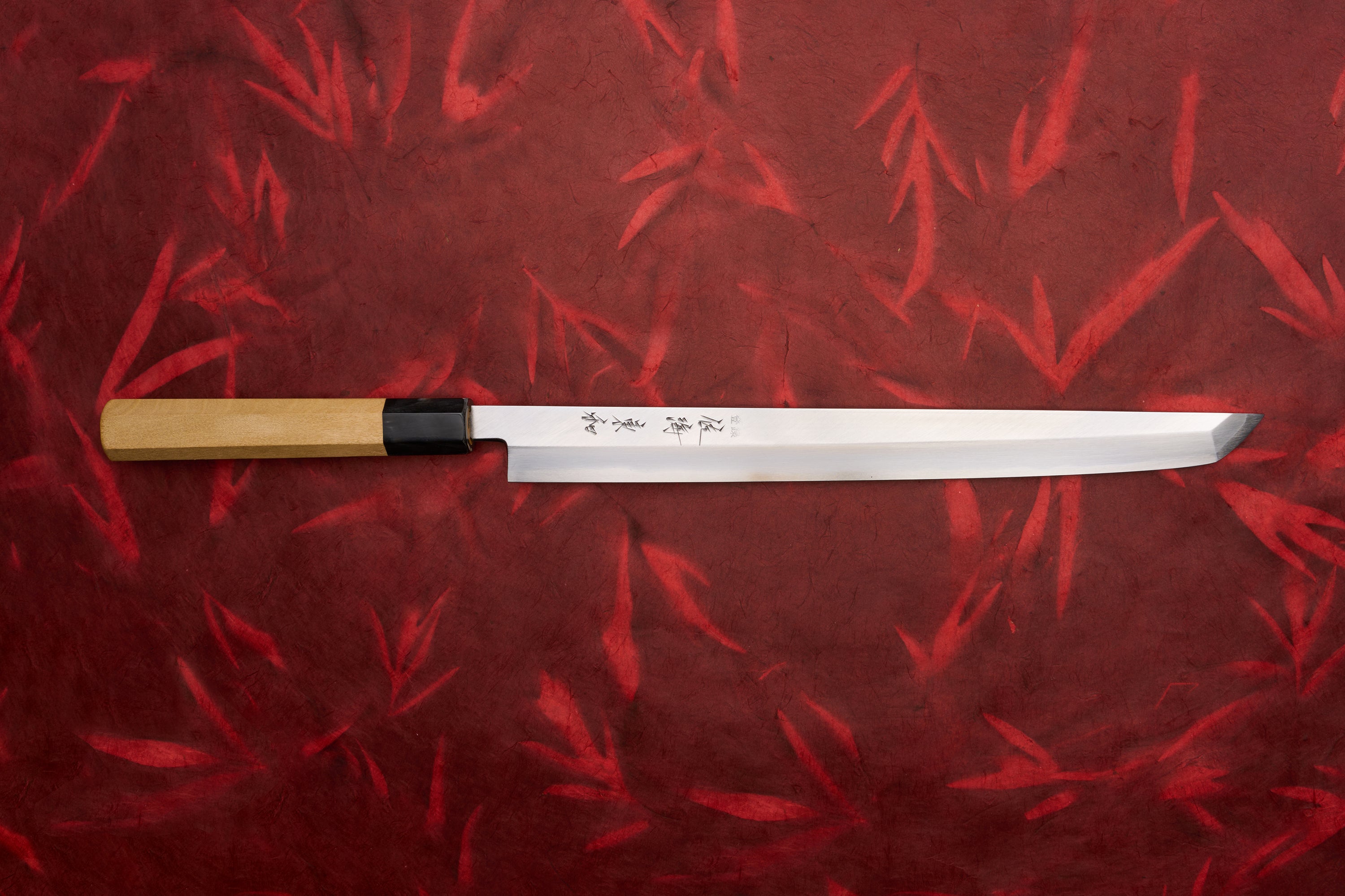 Touroku Sakai Tohwa Shirogami Sakimaru Takohiki 300mm knife, featuring a long, single-bevel blade with Japanese inscriptions and a light wooden handle, set against a bamboo-leaf–patterned background.