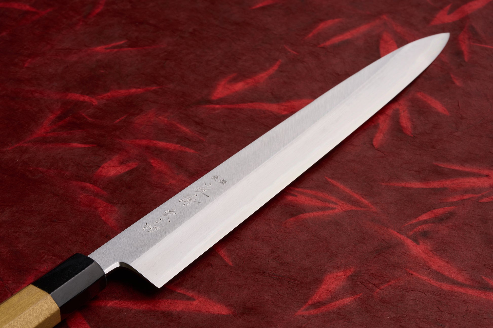 Touroku Sakai Tohwa Shirogami Yanagiba 300mm, a polished steel Japanese slicing knife with an octagonal handle, lies on a red background, showcasing its single bevel edge and engraved characters.