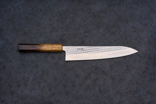 Tsunehisa AUS10 Sanjushichi Nawame Damascus Gyuto 240mm features a Damascus-patterned blade with a maker's mark and an octagonal wooden handle, laid on a textured surface.