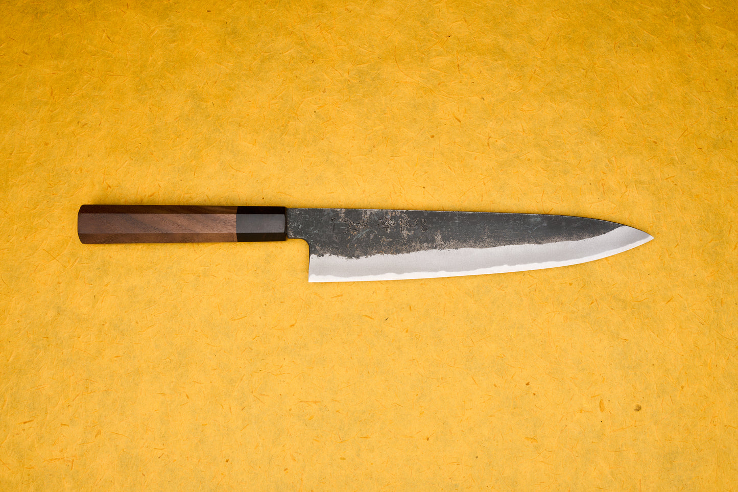 Touroku Sakai Yoshikazu Shirogami Kurouchi Gyuto 240mm, a slender Japanese kitchen knife, features a high-carbon steel blade with a kurouchi finish and a traditional octagonal walnut handle. Ideal for versatile chef tasks.