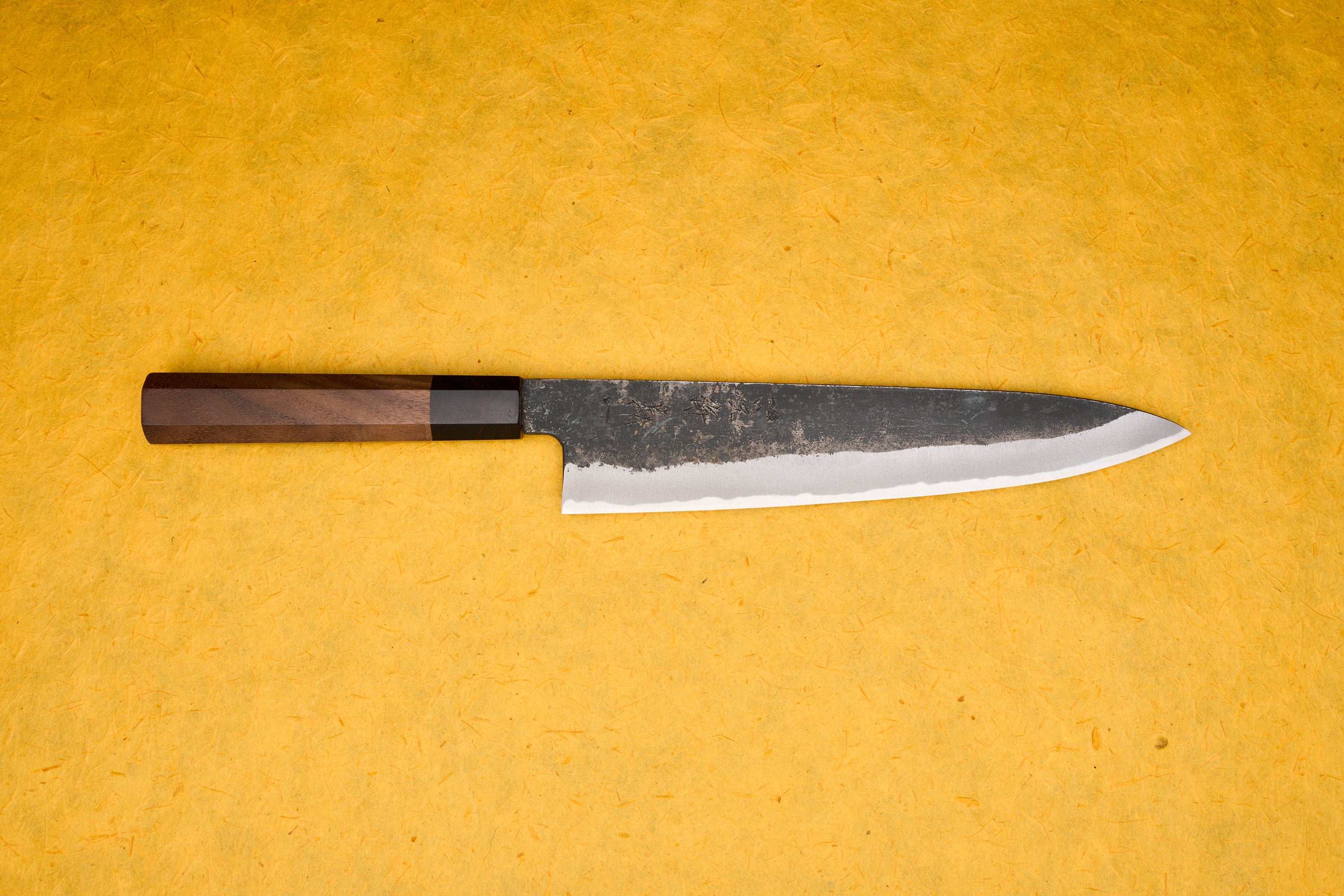 Touroku Sakai Yoshikazu Shirogami Kurouchi Gyuto 240mm, a slender Japanese kitchen knife, features a high-carbon steel blade with a kurouchi finish and a traditional octagonal walnut handle. Ideal for versatile chef tasks.
