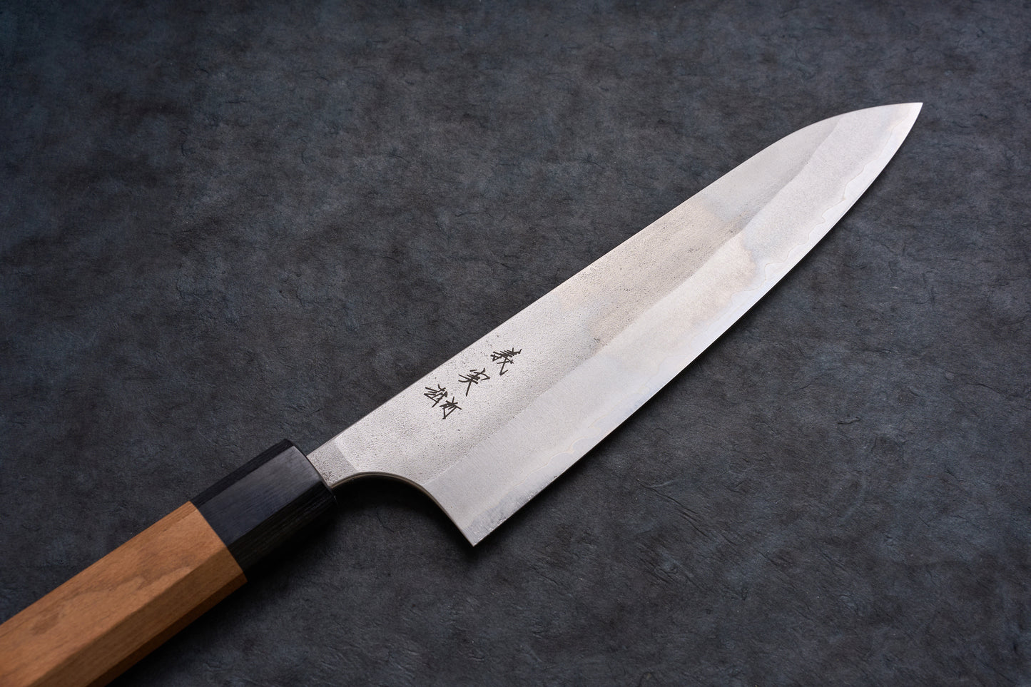 Yoshimi Kato AS/S Nashiji Gyuto 210mm knife with a single-bevel blade, hamon line, kanji markings, and octagonal wooden handle on a textured surface.
