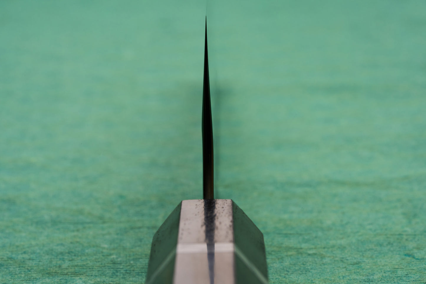Yoshimi Kato SG2 Hyo Gyuto 210mm blade edge stands upright on a green mat, showcasing its precise taper and craftsmanship, embodying the excellence of handcrafted Japanese kitchen knives.