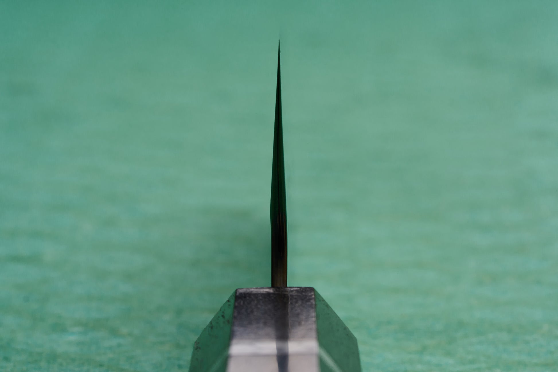 Yoshimi Kato SG2 Hyo Santoku 165mm knife, viewed edge-on, showcasing its razor-sharp blade against a green background, epitomizing the excellence of Japanese craftsmanship from Knifewear.
