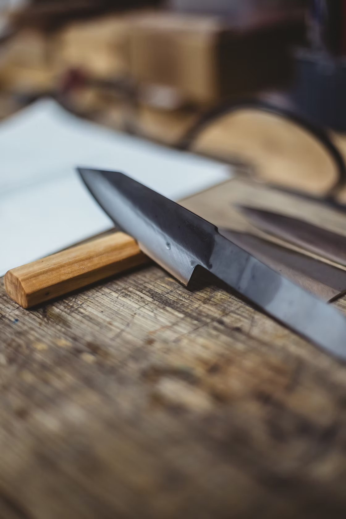 Resqknives Korpi Camp Kitchen Knife blade on a wooden workbench, showcasing the high-quality recycled Finnish stainless steel, with a wooden handle blank visible underneath.