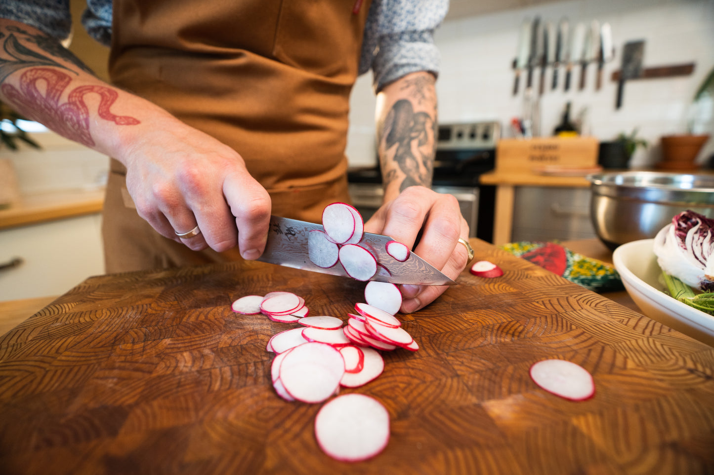 Close-up of tattooed hands slicing radishes with a Japanese chef’s knife during the Kitchen Knife 101 — InglewooDIY workshop.