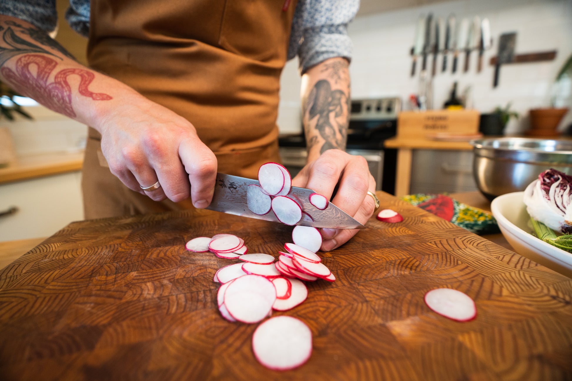 Close-up of tattooed hands slicing radishes with a Japanese chef’s knife during the Kitchen Knife 101 — InglewooDIY workshop.
