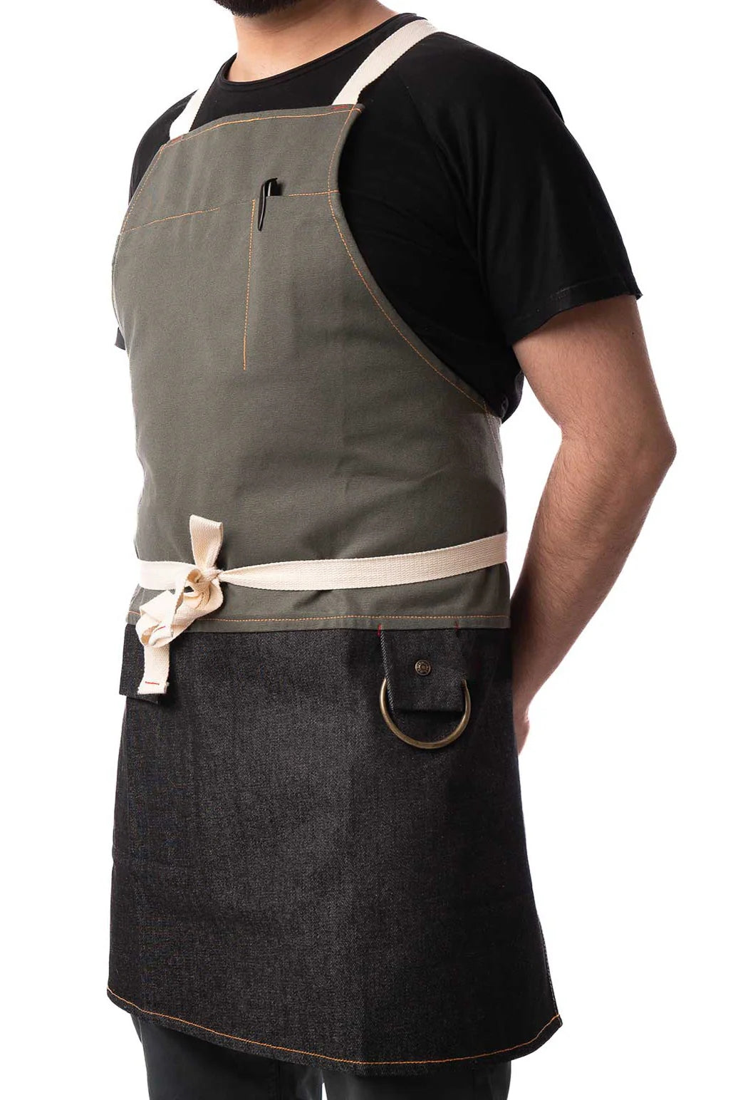 Person wearing Medium Rare Old Fashioned Apron with olive-green bib, denim lower half, crossback straps, pen pocket, lap pocket, and brass D-ring.