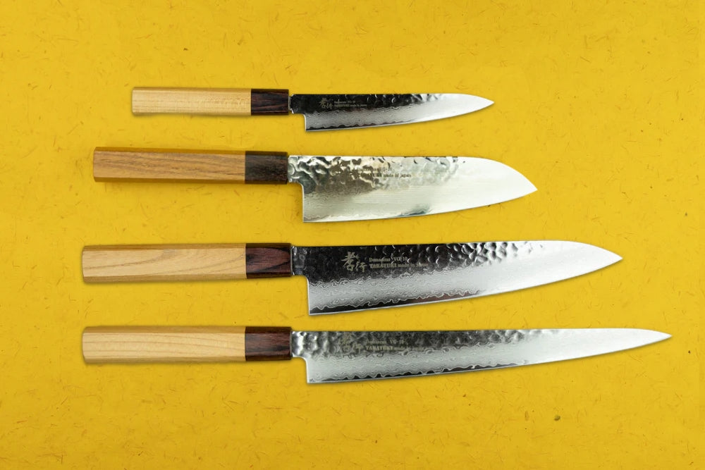 Sakai Takayuki VG10 33 Layer Damascus 4 Piece Knife Set displayed on a yellow surface, featuring hammered stainless blades and two-tone wooden handles, showcasing precision craftsmanship and elegant Japanese design.